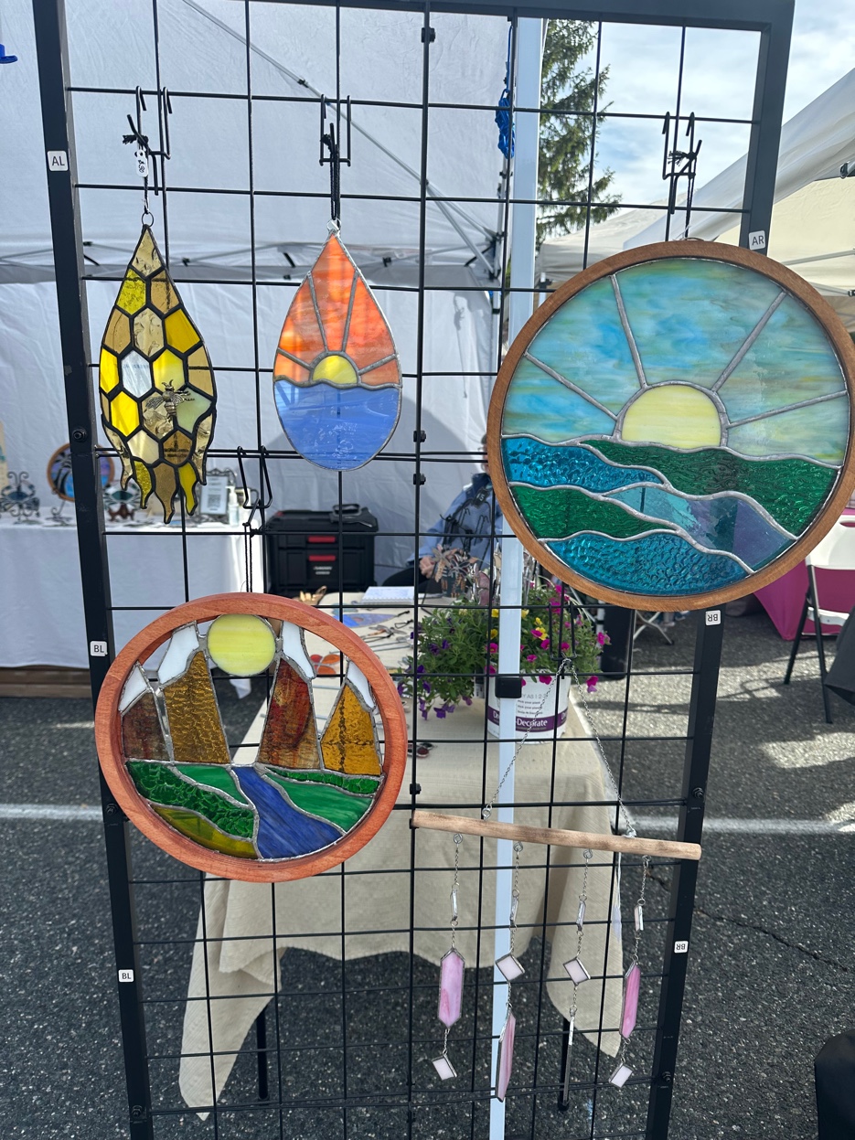 Stained glass roundels and suncatchers displayed on a wire rack at a craft show